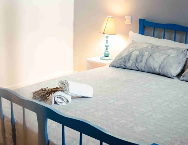 detalle cama sabanas grises con cama de barrotes de madera azul , lampara azul