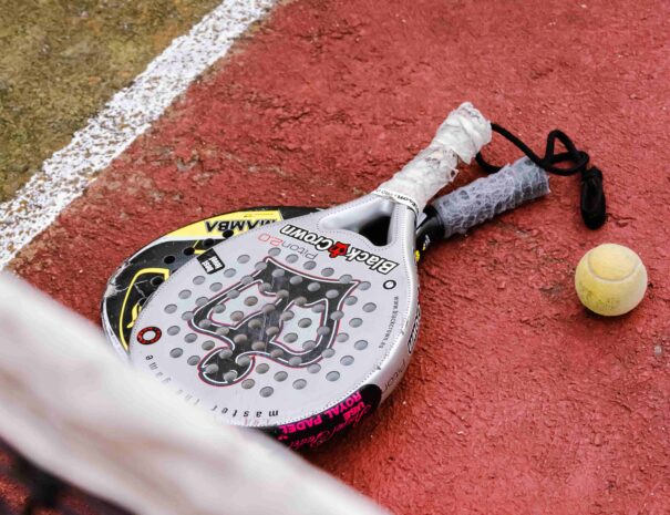 dos raquetas de padel en el suelo junto pelota tennis en pista de tennis y red difuminada