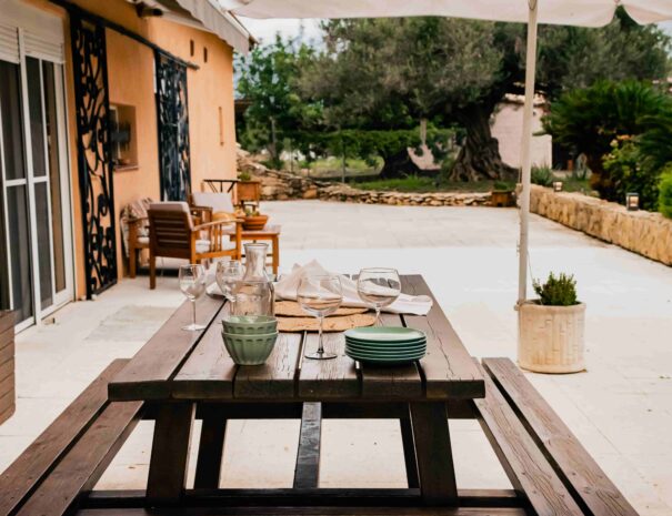 mesa de picnic con platos y vasos, sombrilla, en una gran terraza de suelo blanco, rejas en ventanales diseño arábico